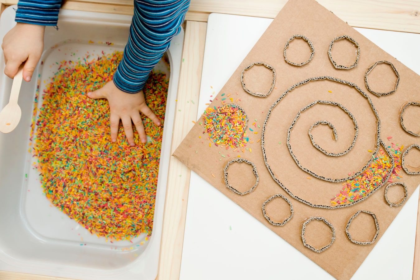 Kinderhände lernen eine neue Textur kennen – bunte Bonbons und Streusel, daneben befindet sich ein DIY-Labyrinth aus Karton